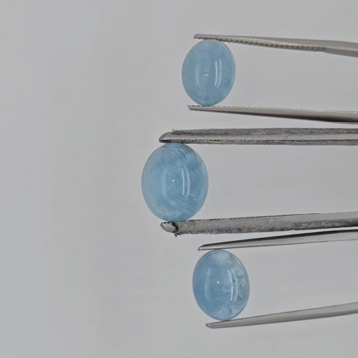 Video of three blue cabochon gemstones in tweezers against a white background