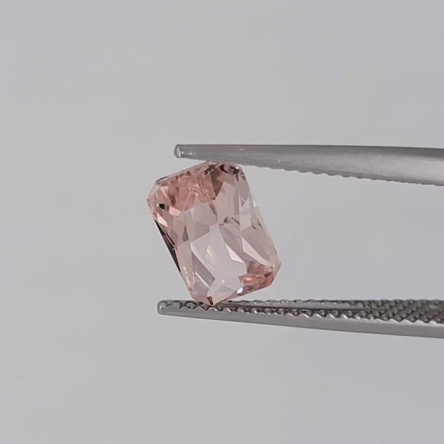 Video of a radiant cut pink gemstone in tweezers against a white background