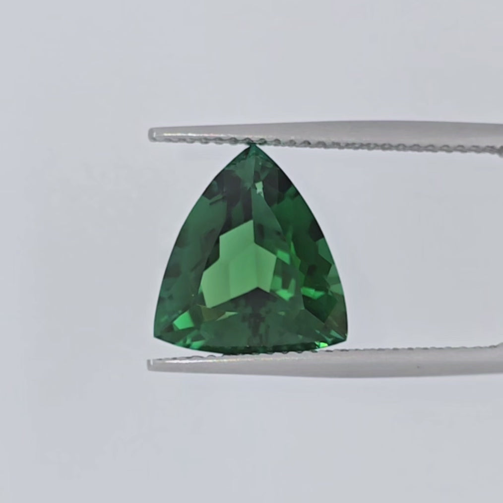 Video of a triangular green stone shown in a pair of tweezers
