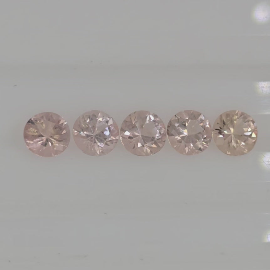 Video of five round brilliant cut orangy pink to pinkish orange gems on a white background.
