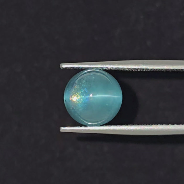 video of a turquoise blue cat's eye cabochon being displayed in tweezers on a black background.