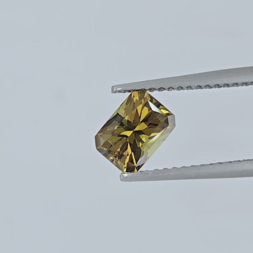 Video of Golden gem being shown in a pair of tweezers on a white background