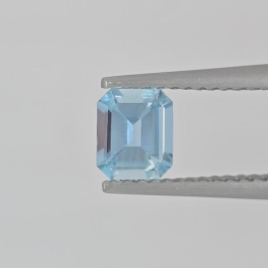 Video of an emerald cut light blue gemstone in tweezers against a light gray background