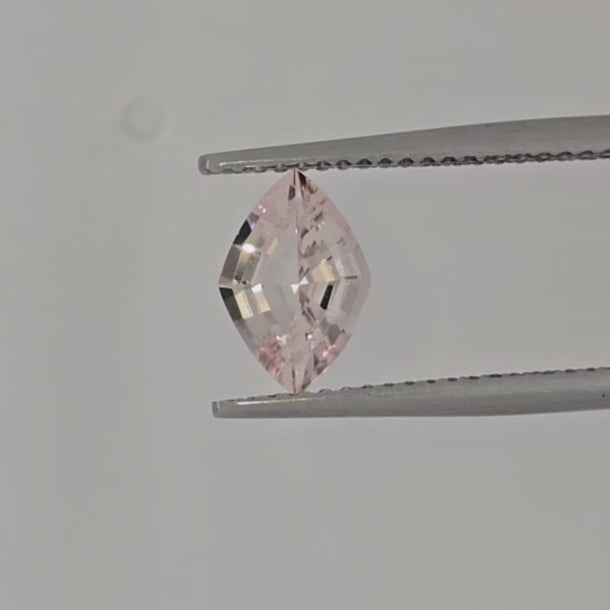 Video of a lozenge shaped pink gemstone in tweezers against a white background