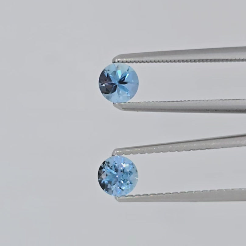 Video of two round blue gemstones in tweezers against a light background
