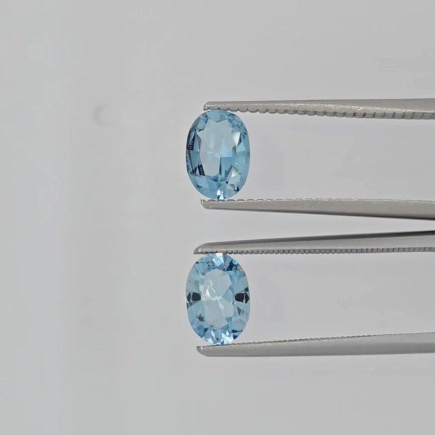 Video of two oval faceted light blue gemstones in tweezers against a light backgorund