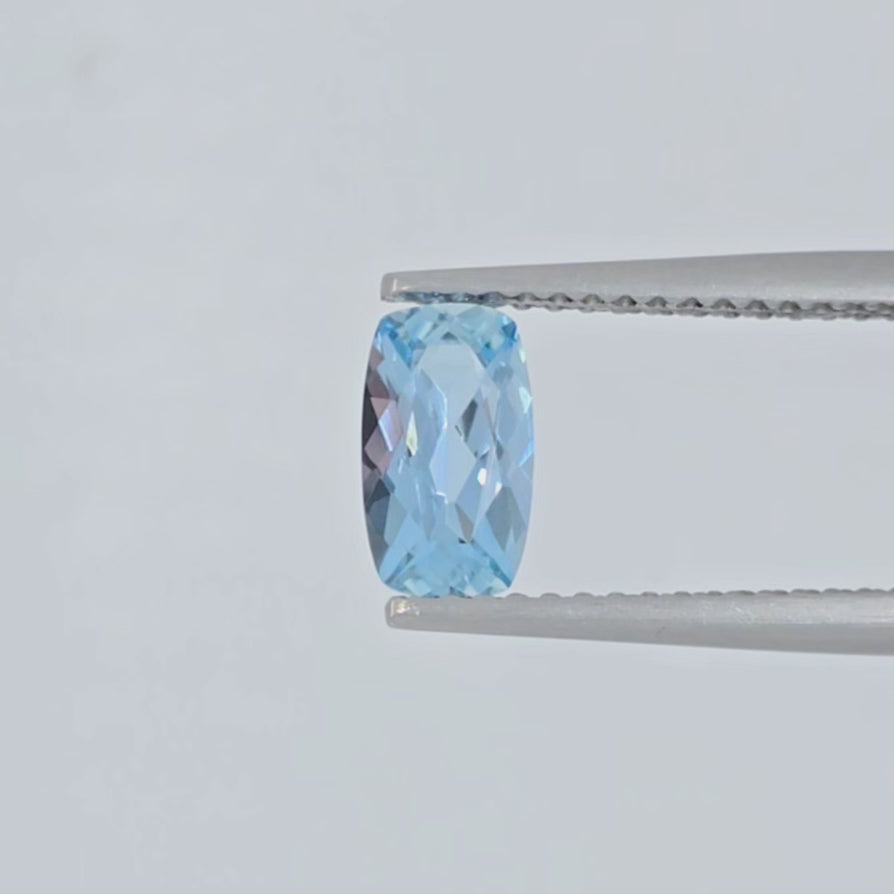 Video of a cushion cut light blue gemstone in tweezers against a white background