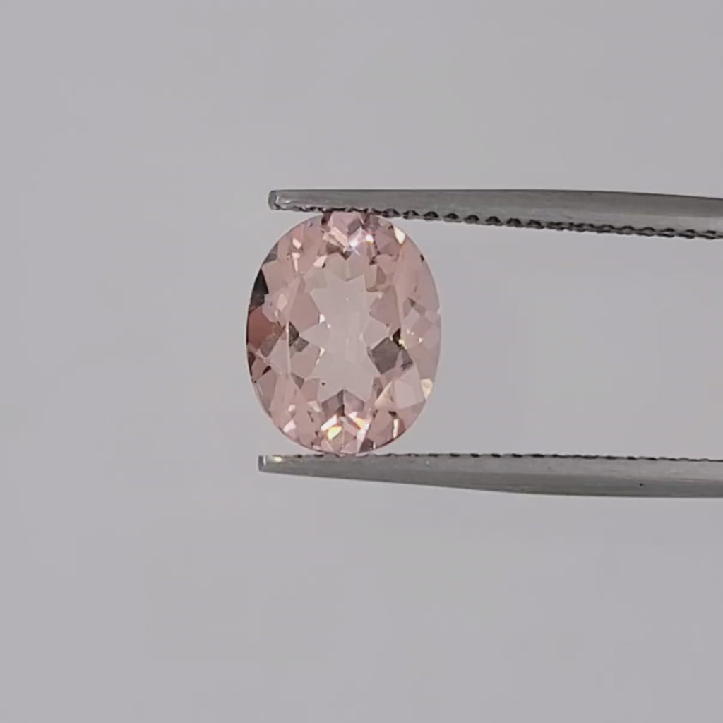 Video of a transparent oval pink gemstone in tweezers on a white baground