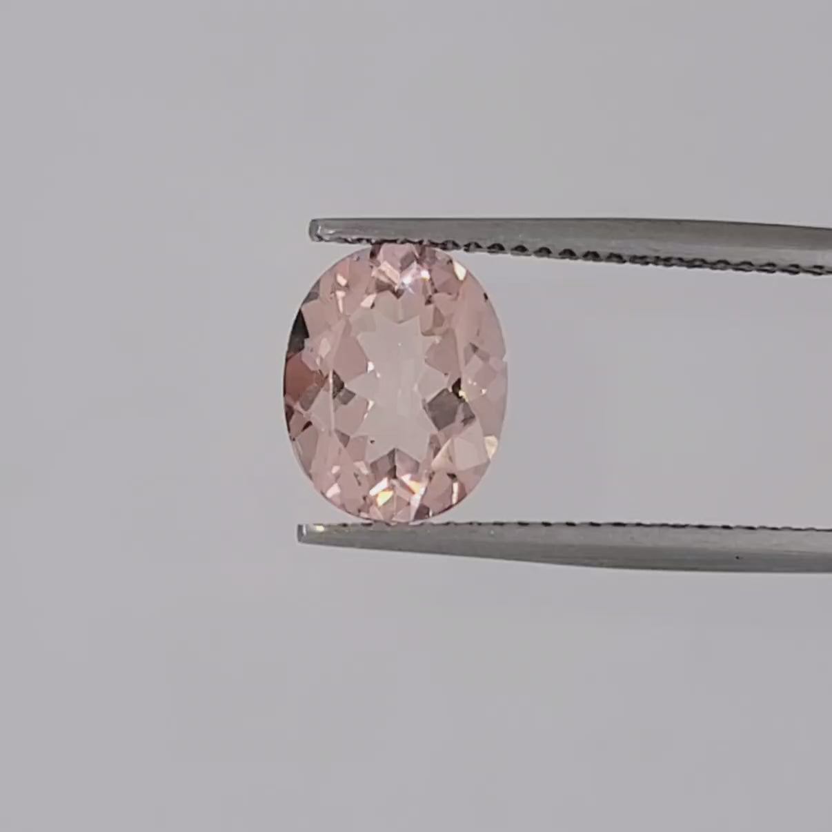 Video of a transparent oval pink gemstone in tweezers on a white baground