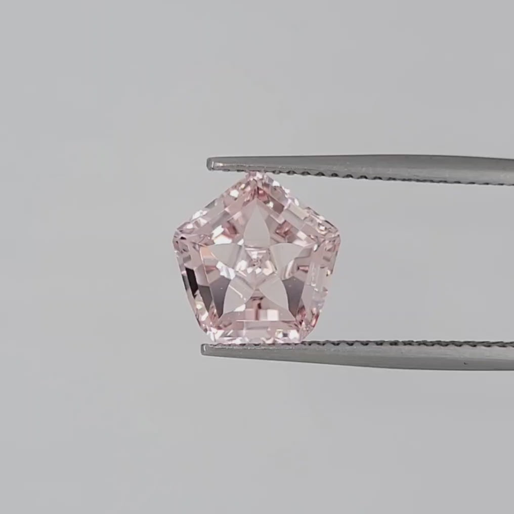 Video of a pink pentagonal gemstone in tweezers against a white background