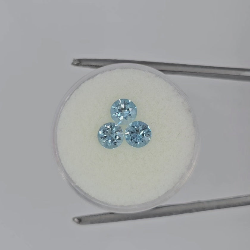 Video of three faceted round light blue gemstones on an off-white round pad in tweezers against a white background