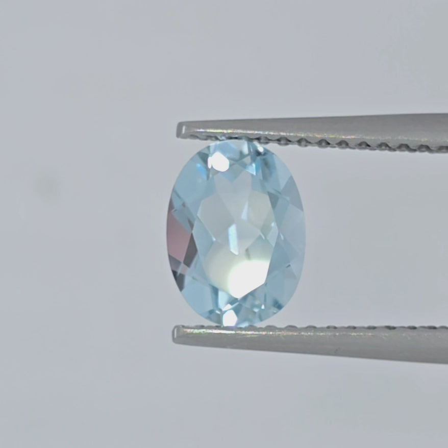 Video of a faceted light blue gemstone oval in tweezers against a white background