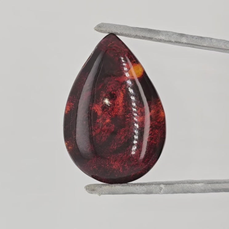 Video of a pear shaped cabochon with natural inclusions in tweezers against a white background