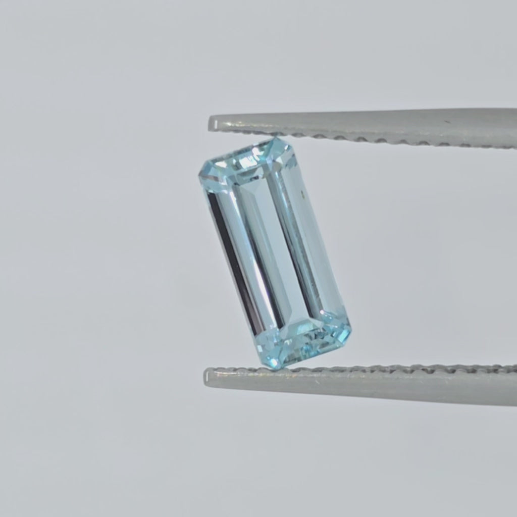 Video of a light blue emerald cut gemstone in tweezers against a light background