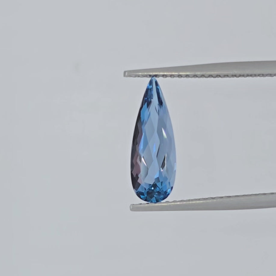 Video of a pear shaped blue faceted gemstone in tweezers against a white background
