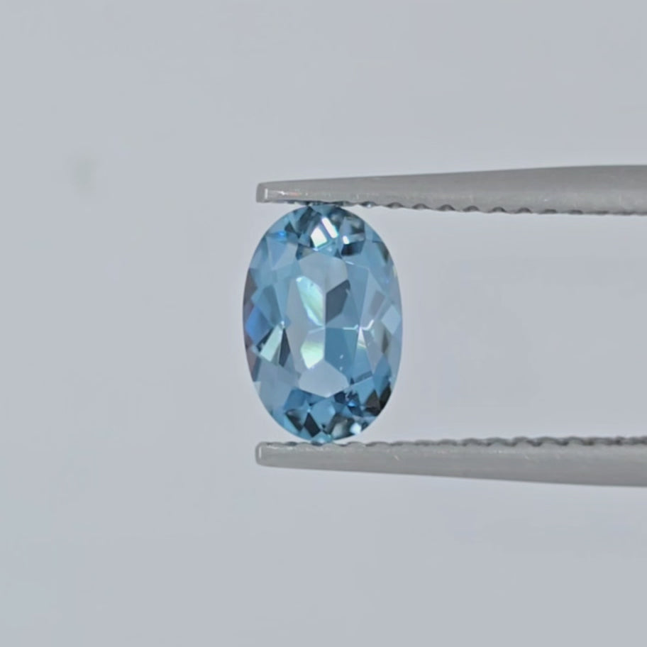Video of a faceted oval blue gemstone in tweezers against a plain white background