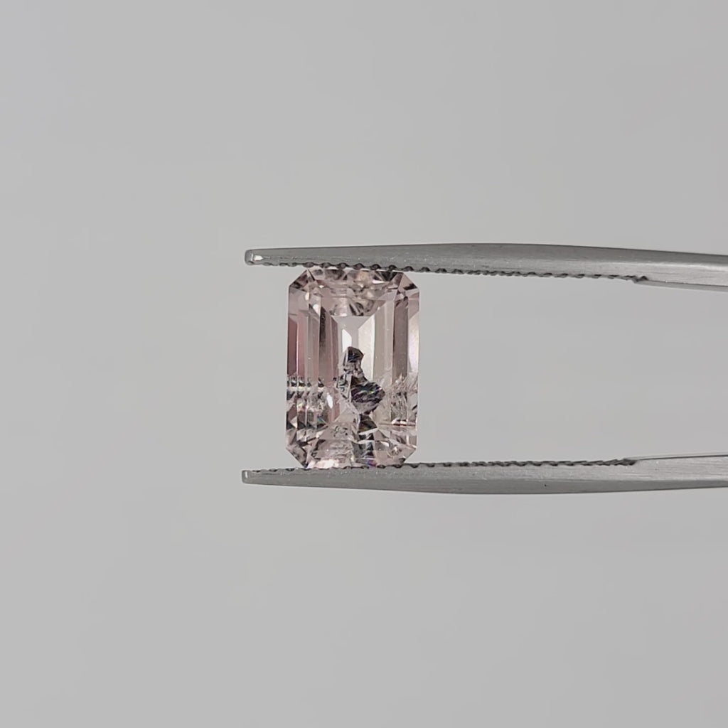 Video of a pink emerald cut gem in tweezers against a white background