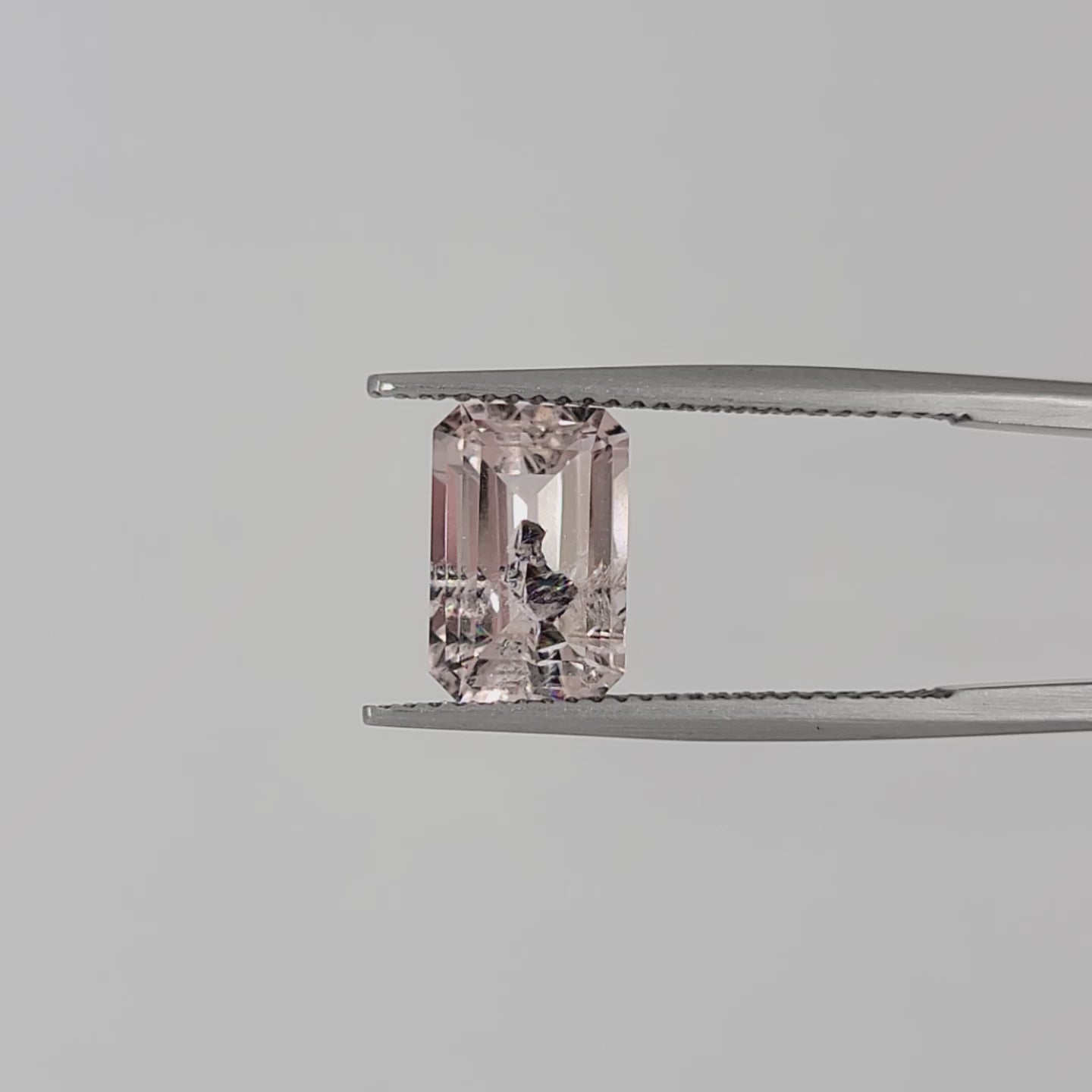 Video of a pink emerald cut gem in tweezers against a white background