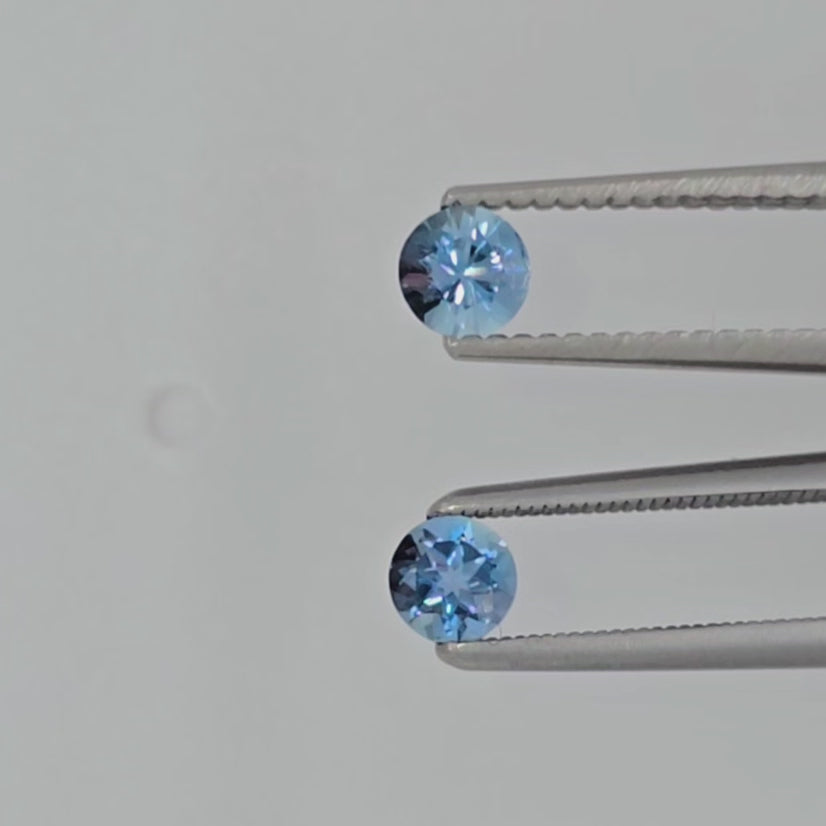 Video of two faceted round blue gemstones in tweezers against a white background