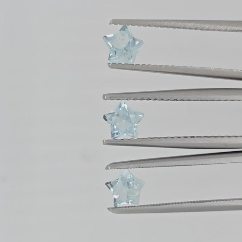 Video of three light blue star shaped faceted gemstones in tweezers against a pale gray background