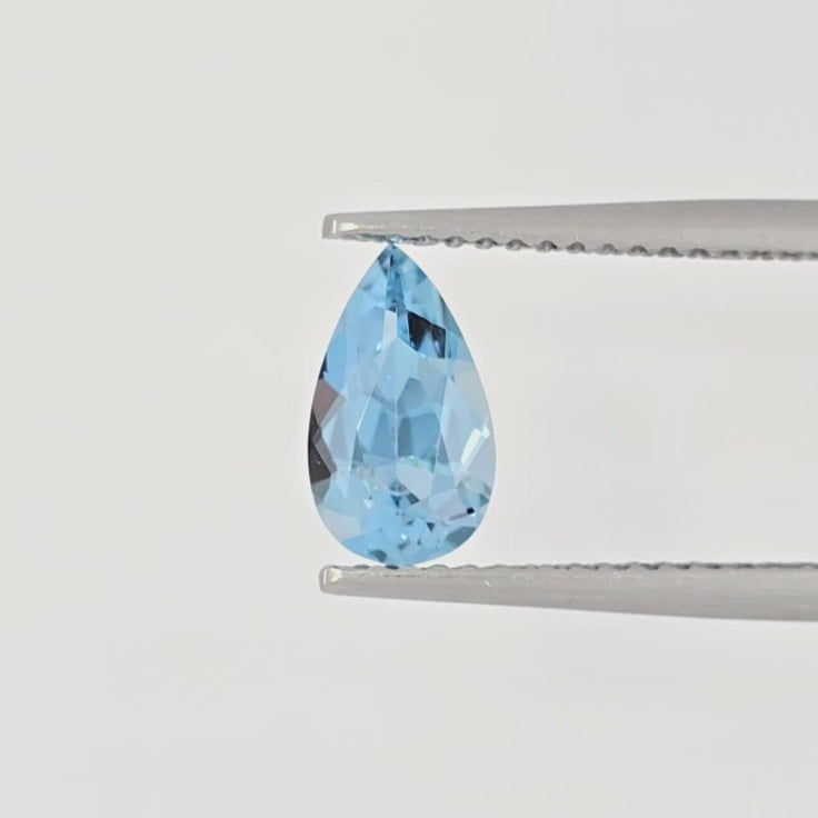 Video of a blue pear shaped faceted gemstone in tweezers against a white background