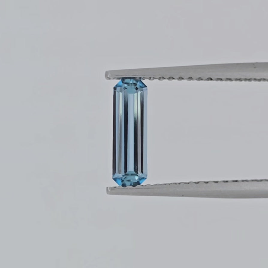 Video of a rectangular blue gemstone in tweezers against a white background