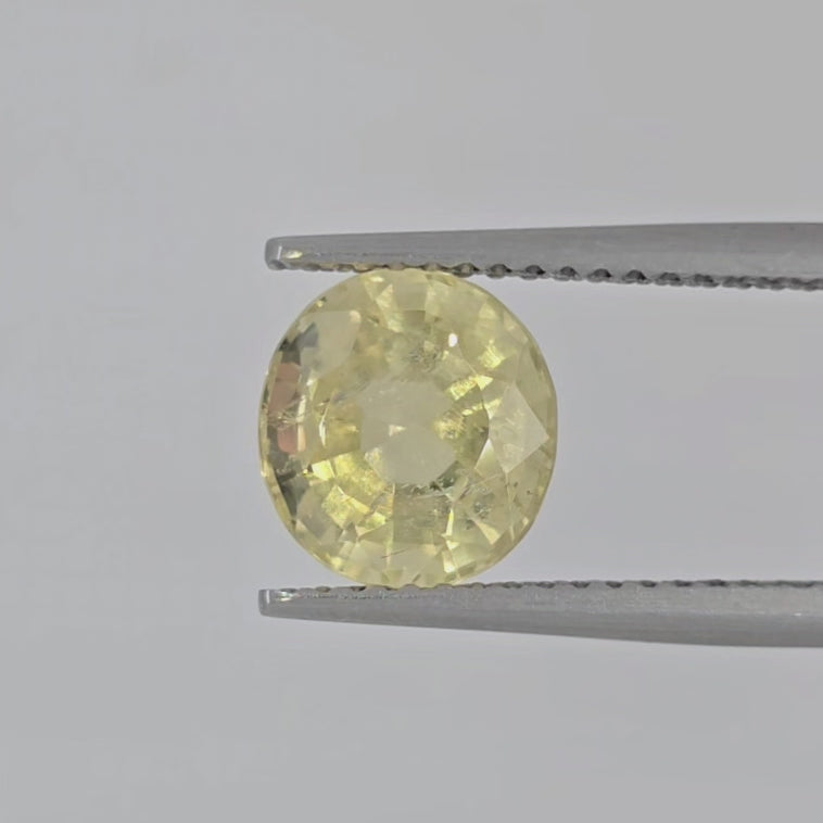 Video of An oval faceted yellow gemstone, likely a shown in a pair of tweezers against a plain white background.