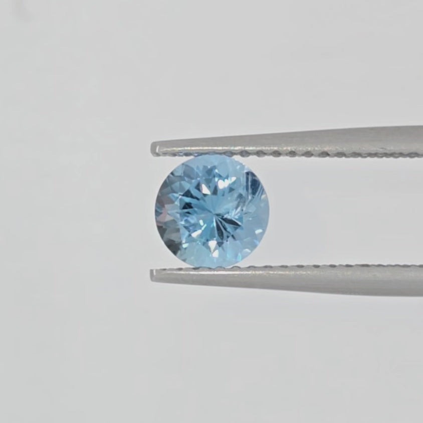 Video of a light blue round brilliant cut gemstone in tweezers against a plain white background