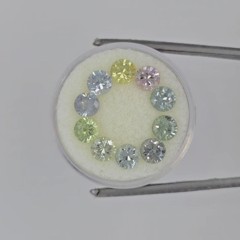 Video of ten faceted round gemstones arranged in a circle on a white background, showing a mix of silver, green, pink, and yellow tones.