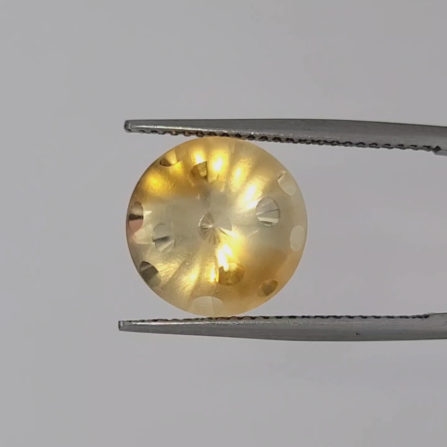 Yellow and white gemstone displayed in tweezers