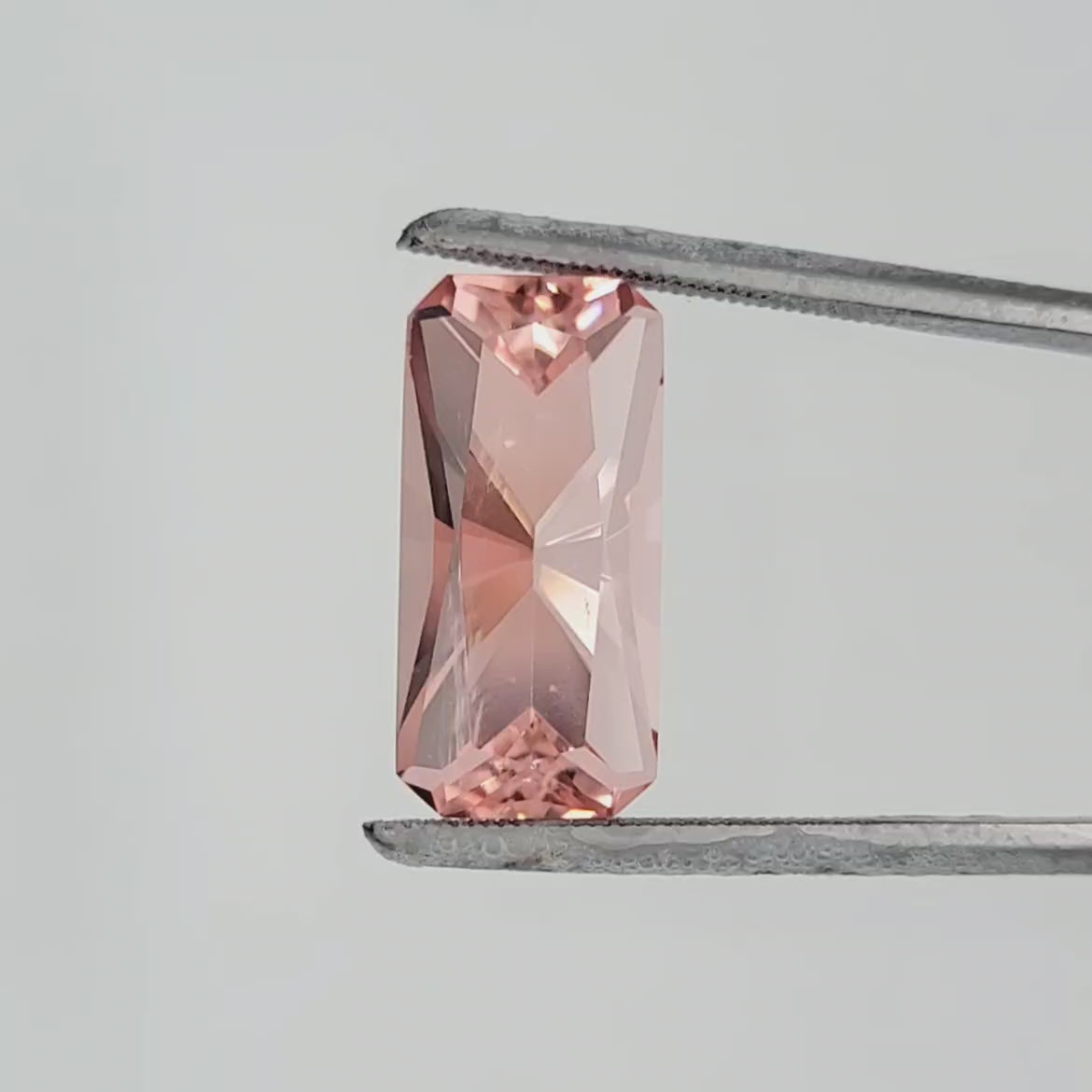 Video of a rectangular radiant cut pinkgemstone in tweezers against a white background