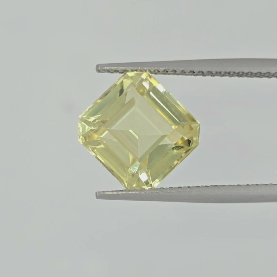 Video of a square cut yellow gemstone in tweezers against a light gray background.
