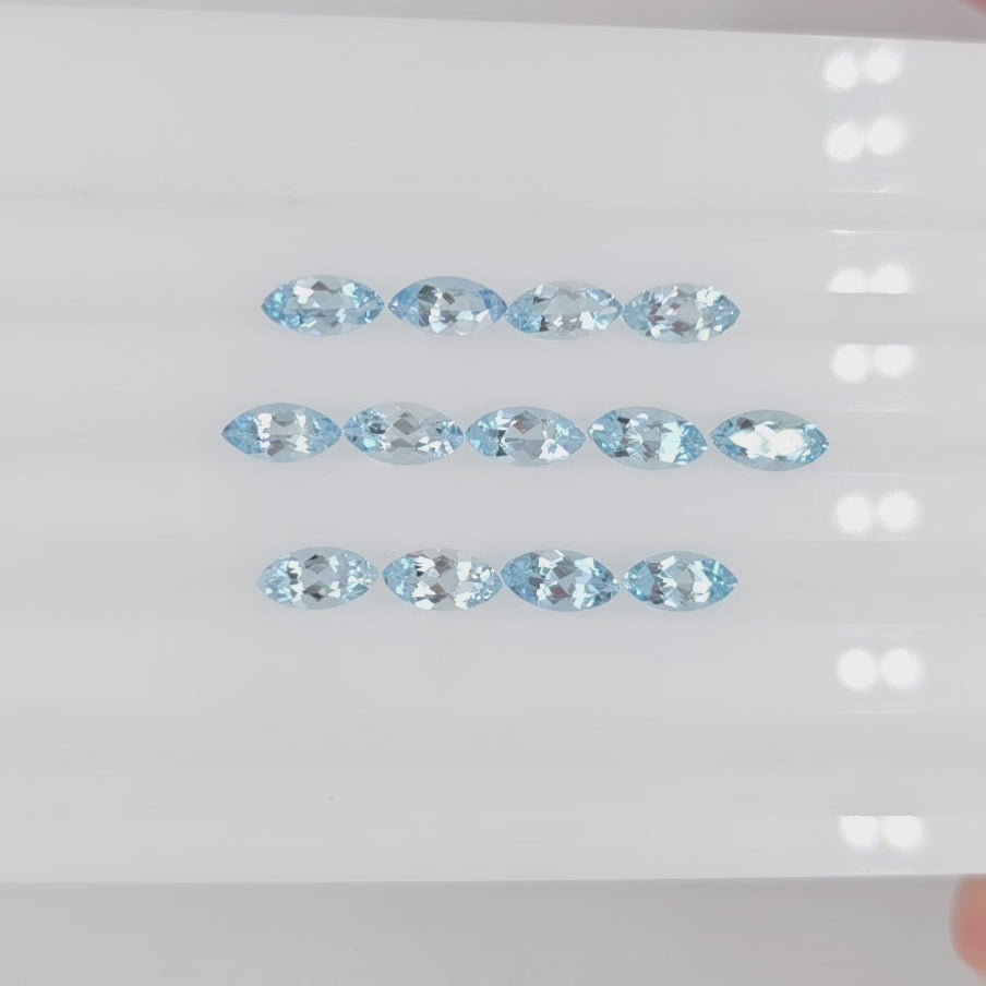 Video of thirteen light blue marquise cut gemstones in three horizontal rows on a  white background
