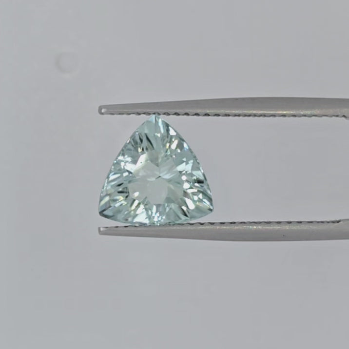 Video of a triangular faceted light greenish blue gemstone in tweezers against a plain white background