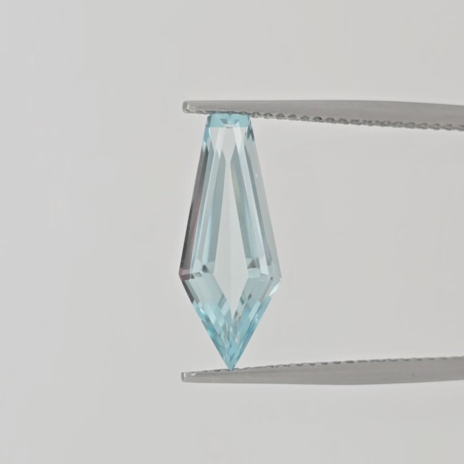 Video of a faceted light blue gemstone with an elongated kite shape in tweezers against a plain white background