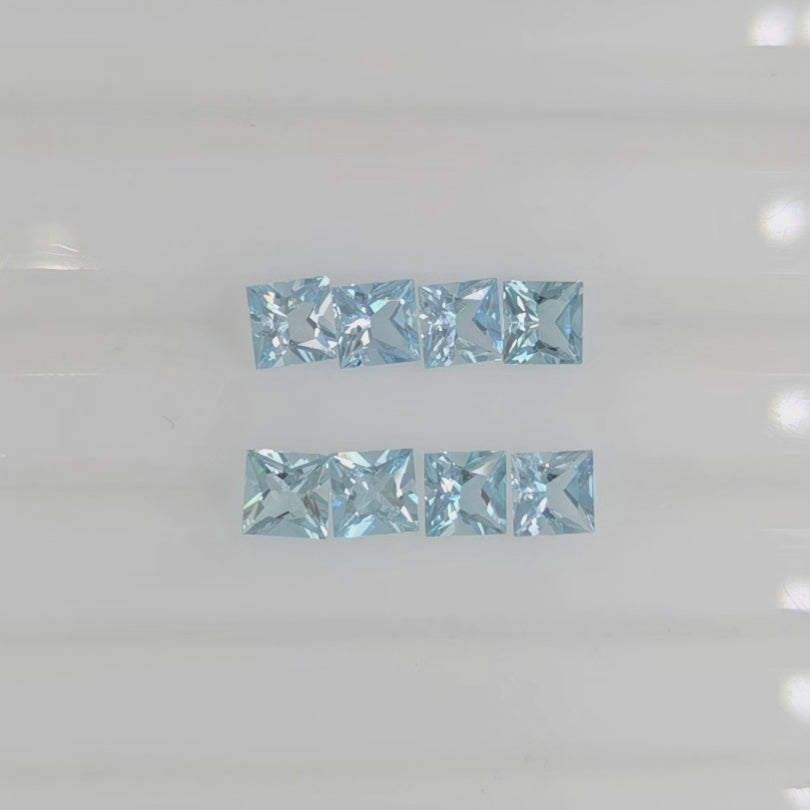 Video of eight square faceted light blue gems arranged in two rows against a plain white background. 
