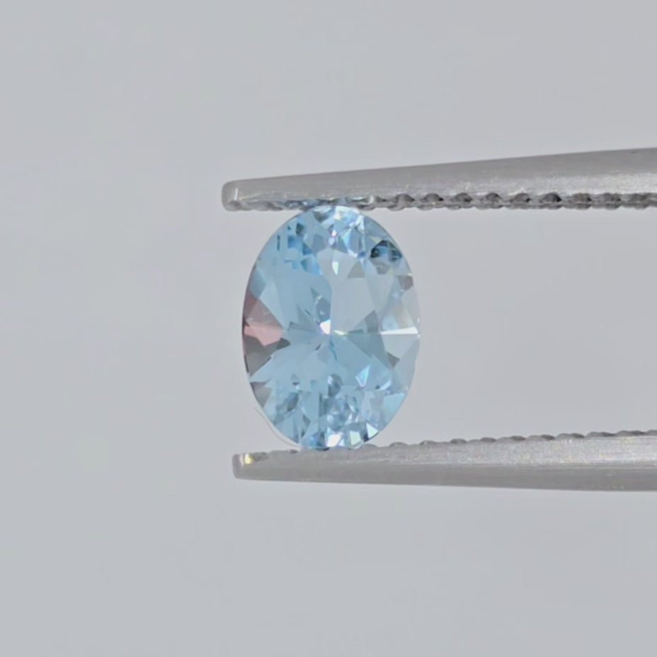 Video of a light blue faceted oval gemstone in tweezers against a white background