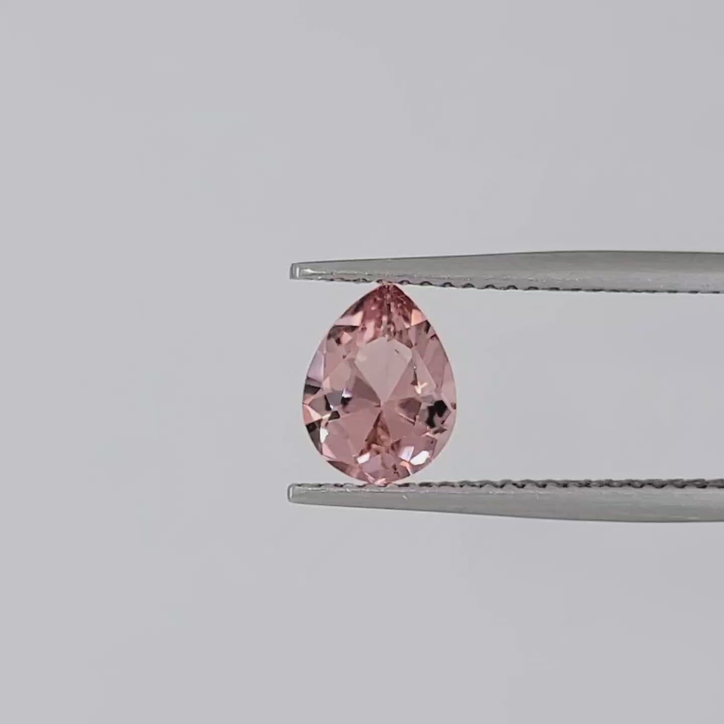 Video of pear shaped pink gemstone in tweezers against a white background