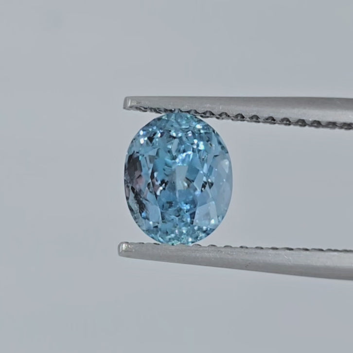 Video of an oval faceted blue gemstone in tweezers against a light gray background