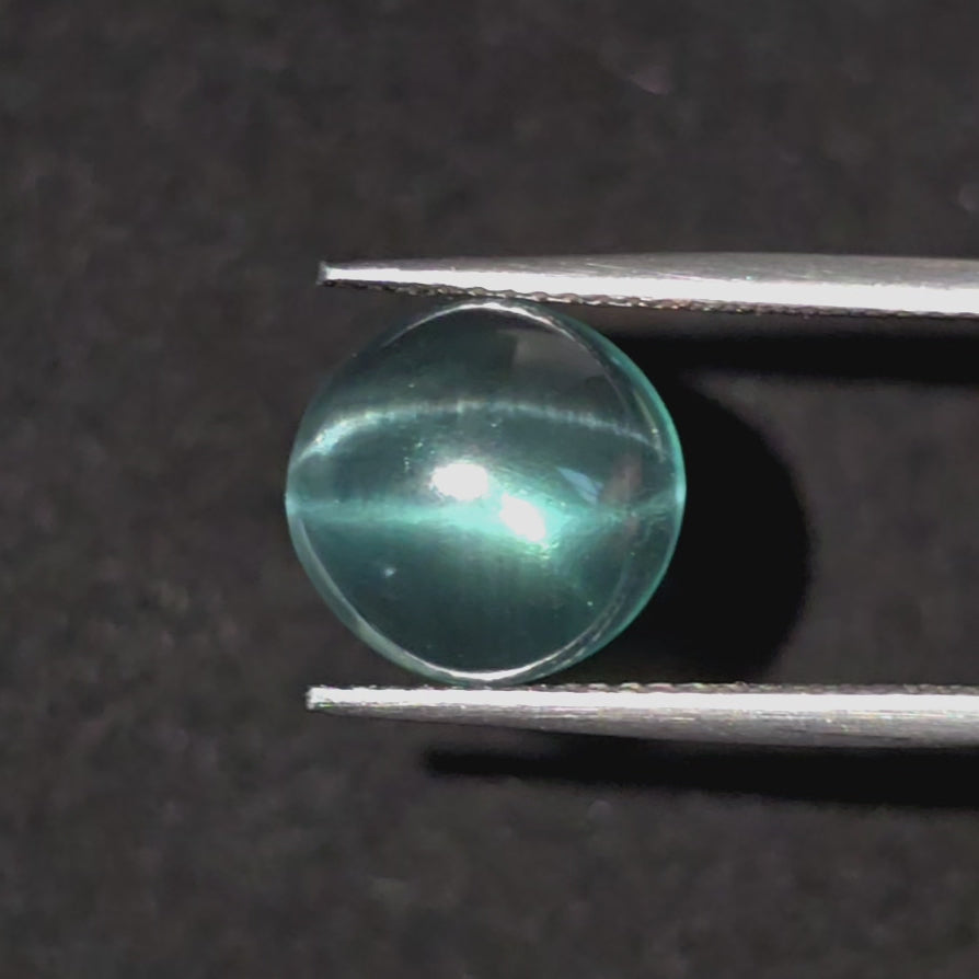 Video of a bluish green cabochon gemstone with a star effect in tweezers  against a black textured background