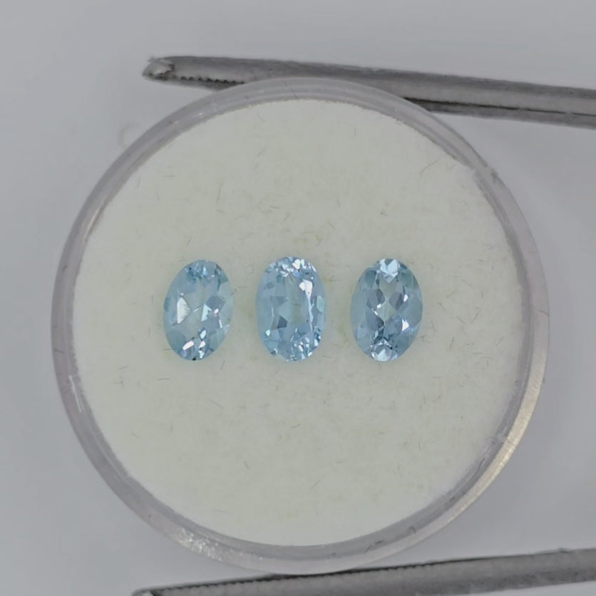 Video of three faceted oval light blue gemstones on a circular white background in tweezers against a pale gray background