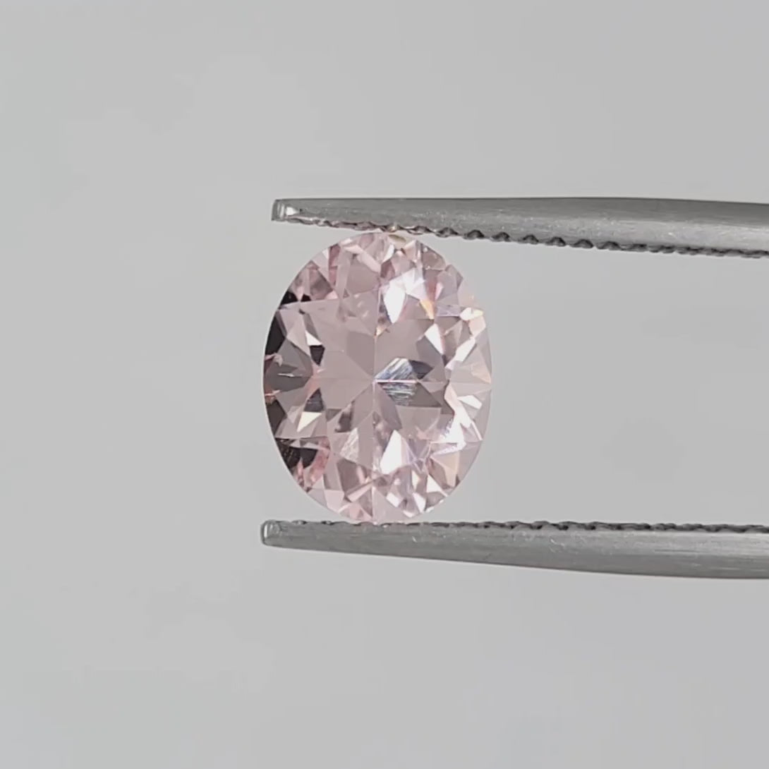 Video of an oval faceted pink gemstone in tweezers against a white background