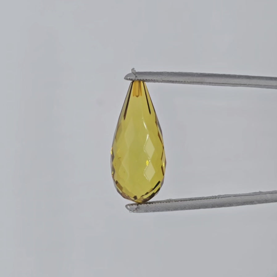 Video of transparent greenish yellow teardrop shaped briolette in tweezers against a light gray background