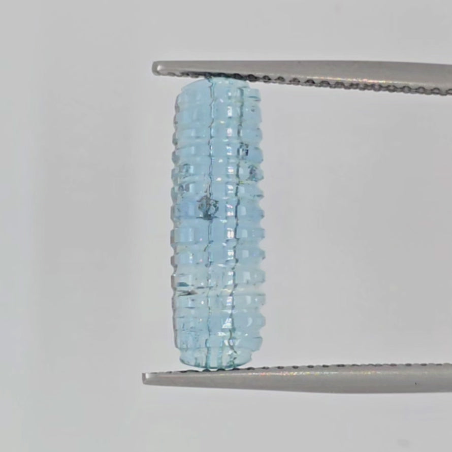 Video of a light blue ribbed gemstone in tweezers against a white background