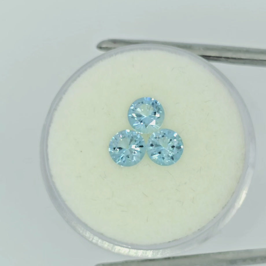 Video of three round brilliant cut light blue gemstones on an off-white round pad in tweezers against a white background