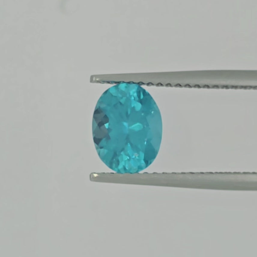 A video of an oval-cut, faceted turquoise gemstone in tweezers shown on a plain light gray background.