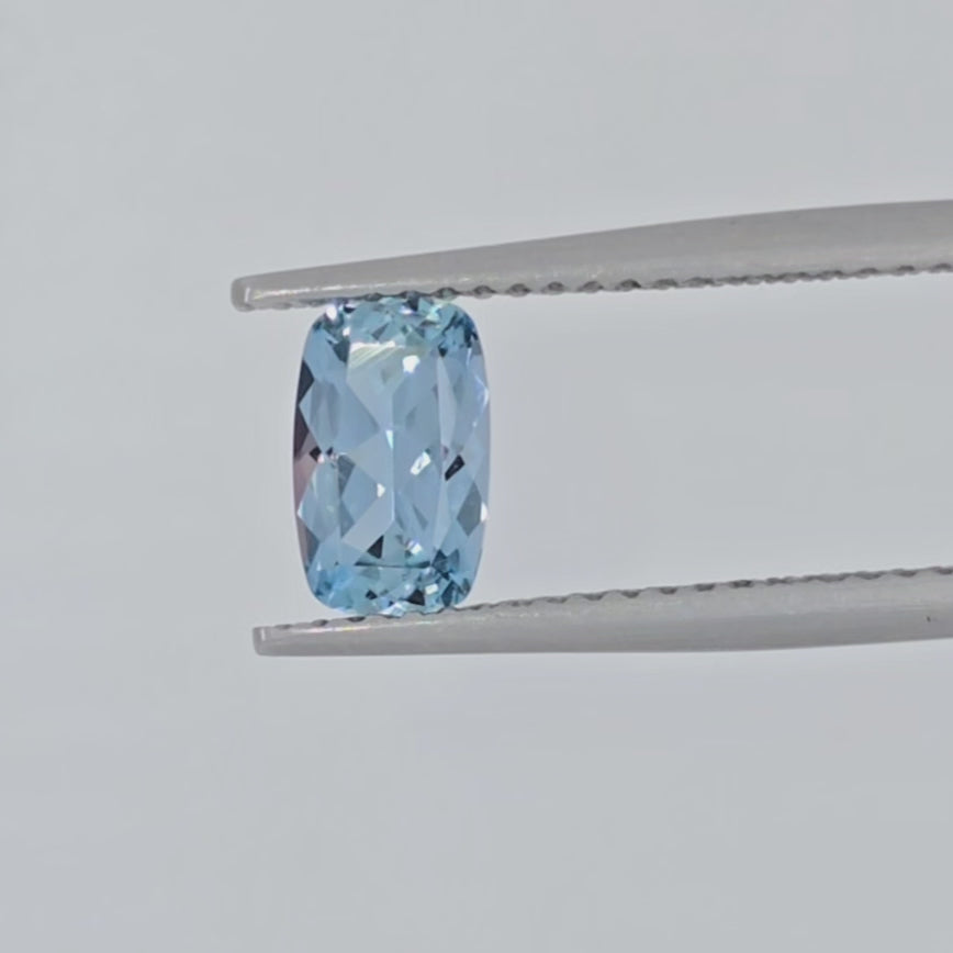 Video of a cushion cut light blue gemstone in tweezers against a white background
