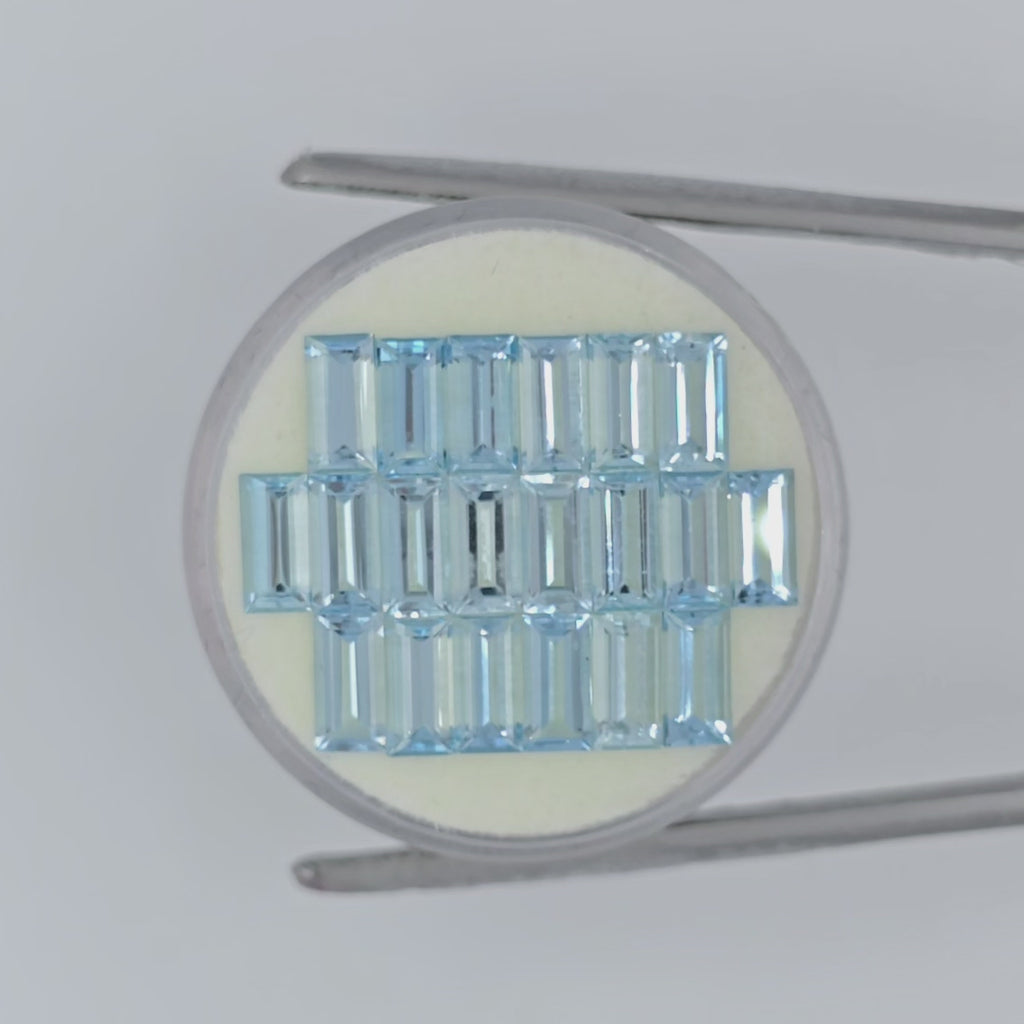video of twenty rectangle cut light blue faceted stones on an off-white circular pad in tweezers on a white background