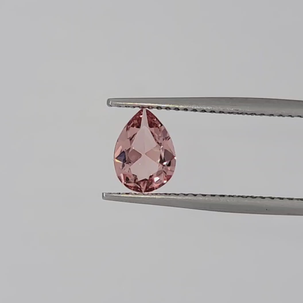 Video of a transparent pink pear shaped gemstone in tweezers against a white background