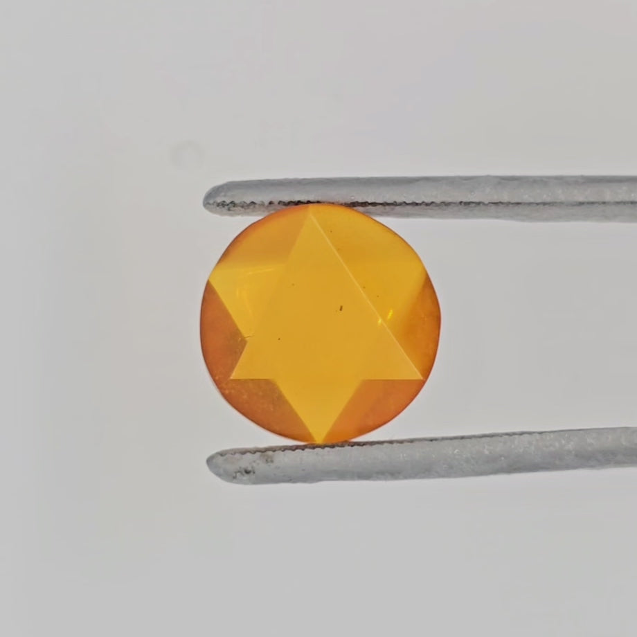 Video of a round orange gemstone in tweezers against a plain light gray bakground